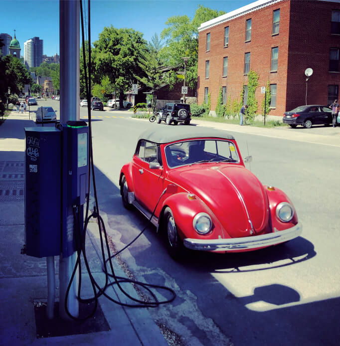 Une Beetle modifiée en véhicule électrique se faisant charger dans la rue.